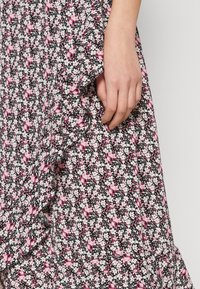 Vestido floral con fondo negro, pequeñas flores blancas y rosas, dobladillo con volantes y un diseño fluido. Tela de algodón, textura suave.