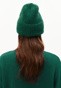 Groene gebreide muts met een gestructureerde afwerking, voorzien van een geribde rand en een afgeronde bovenkant, gedragen over lang bruin haar.