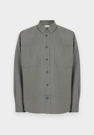 Pelēka kokvilnas maisījuma auduma krekla krekls ar pogām. Tam ir klasiskas apkakles, divas krūšu kabatas un priekšējā pogu aizdare.