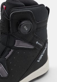 Botte de randonnée waterproof noire avec un dessus texturé, accents gris et système de laçage BOA. Dotée d'un matériau respirant et d'une semelle en caoutchouc blanche.