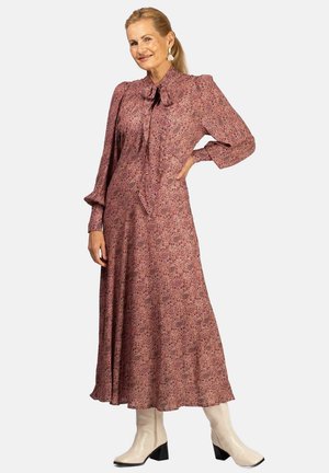 Langärmliges Kleid mit hohem Kragen in Pink mit filigranen Blumenmustern. Weicher, fließender Stoff und Bindedetail am Kragen. Getragen mit beigen Stiefeln.