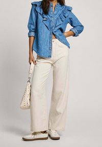 Camisa de denim con cuello rizado, combinada con pantalones de pierna ancha de rayas color crema. Zapatillas blancas y un bolso crema con acentos de tachuelas.