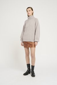 Maglione oversize grigio chiaro con collo alto, abbinato a una mini gonna in pelle marrone aderente. Modella con stivaletti neri.