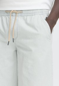 Pantaloni corti leggeri color grigio chiaro con vita elasticizzata, cordino regolabile, tasche laterali e una finitura liscia e strutturata.