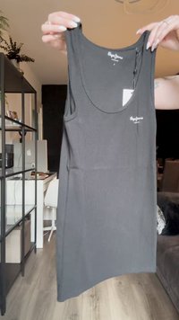 Black ribbed tank top with wide armholes and a scoop neckline. Features a small brand logo on the front. Smooth texture.