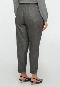 Grijze, geweven broek met een ontspannen pasvorm, voorzien van een elastische tailleband en opgerolde manchetten, gecombineerd met zwarte, open teen haksandalen.