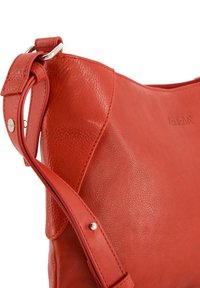 Sac à épaule en cuir rouge avec une texture lisse, des détails de grain subtils et une sangle ajustable fixée par du matériel en métal.