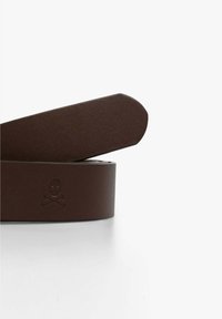 Cinturón de cuero marrón con una textura suave y punta redondeada. Presenta un sutil detalle de calavera y huesos cruzados grabado en el costado.