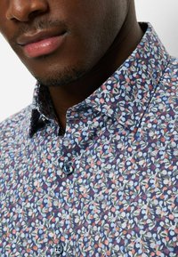 Blaues Hemd mit Blumenmuster, verziert mit kleinen mehrfarbigen Blättern und Beeren. Verfügt über einen klassischen Kragen und zwei schwarze Knöpfe an der Knopfleiste.