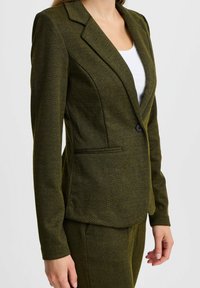 Grüner Chevron-Blazer mit geknöpften Revers, einem einzigen Knopfverschluss und frontalen Taschen. Aus strukturiertem Gewebe gefertigt für eine strukturierte Passform.