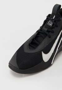 Chaussure de sport noire avec le swoosh blanc de Nike, design à lacets et empeigne en mesh respirant vue de l'angle avant latéral.