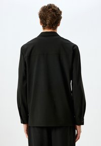 Schwarzes Langarmshirt mit geradem Schnitt. Mit klassischem Kragen, knöpfbaren Manschetten und glattem, strukturiertem Stoff.