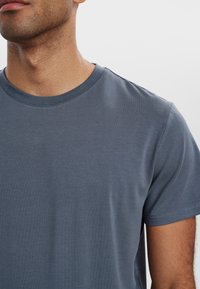 Grå bomulds t-shirt med rund halsudskæring, korte ærmer og glat tekstur. Sømdetaljering er minimal, hvilket giver et rent design.