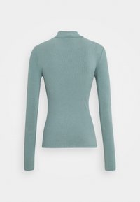 Stretchig, långärmad ribbad tröja i dämpad teal, visad bakifrån, med en liten hög krage.