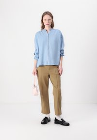 Lyseblå knappekrage skjorte med lange ermer, khakibukser, svarte loafers, hvite sokker og en liten rosa veske. Minimalistisk design.