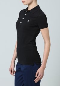 Schwarzes Poloshirt aus Baumwollmaterial mit tailliertem Schnitt, kurzen Ärmeln, Drei-Knopf-Leiste und gesticktem Logo auf der linken Brust.