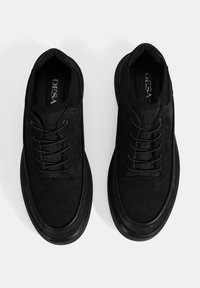 Black sneakers with a textured upper, rounded toe, and flat rubber sole. Features lace-up design and logo inside the shoe.