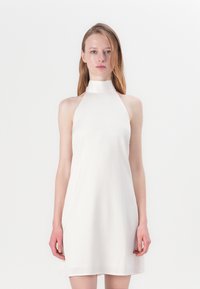 Halteris tipa, bez piedurknēm, baltas krāsas kleita; gluda tekstūra, A formas siluets, ar augstu apkakli un ceļgala garuma apakšmalu. Minimālistisks dizains.