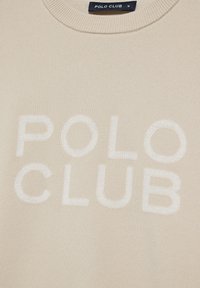 Beige tröja med strukturerad stickning och vit text "POLO CLUB" över framsidan. Rund halsringning och storleksmärke synligt.