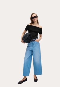 Top negro off-the-shoulder, vaqueros anchos de color azul claro, bolso tejido negro y zapatos planos negros; gafas de sol grandes y pendientes.