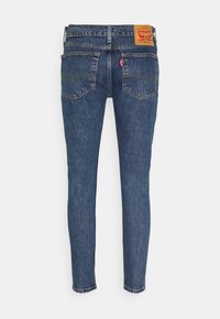 Jeans de denim azul ajustados con una etiqueta trasera de cuero, cinco bolsillos, costuras amarillas y un lavado ligeramente desteñido para un aspecto texturizado.