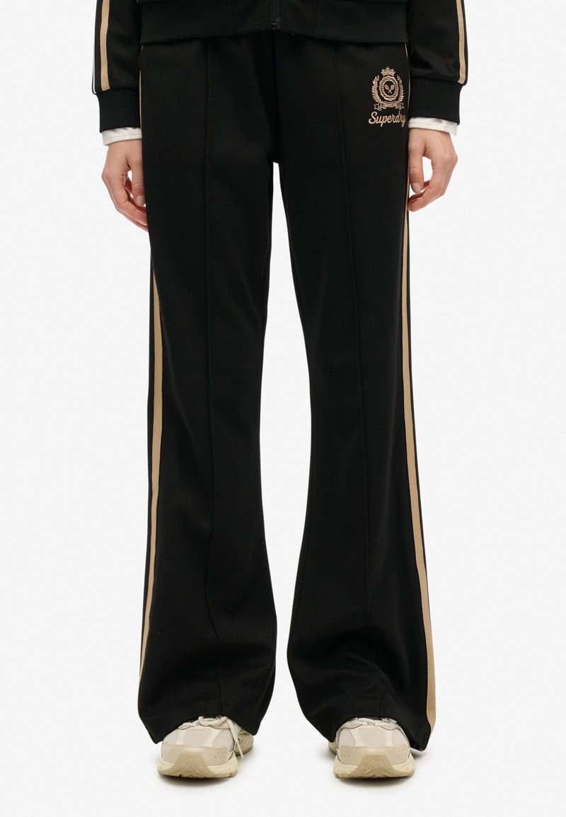 Sorte sweatpants med en flagrende design, der har beige sidelister og et broderet logo på venstre lår. Blødt, komfortabelt stof.