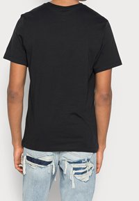 Svart bomullströja med korta ärmar och rund halsringning, i kombination med slitna ljusblå denimjeans med fransade detaljer.