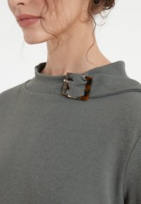 Gray top with a mock neckline featuring a tortoiseshell buckle detail. The fabric is textured with a soft, smooth finish.