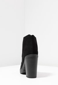 Botines de ante negro con tacón texturizado, forma redondeada y una plataforma contrastante. Detalle de costuras visible en la parte trasera.