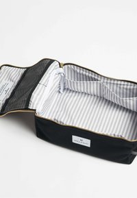 Bolsa de tela negra con cremallera dorada, que cuenta con un forro interior a rayas y un pocket de malla. La etiqueta en el lado dice "SOULEWAY."