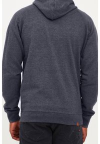 Sudadera gris oscuro de tela suave y texturizada. Presenta un bolsillo canguro, puños y dobladillo acanalados, con un pequeño detalle del логотипo de cuero.