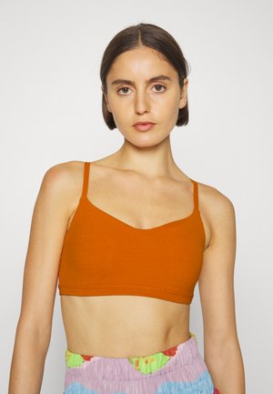 Bralette laranja sem costura com alças largas e decote em V, apresenta um ajuste justo e textura suave. Combinado com calções de pastel estampados.