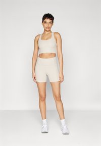 Beige treningssett med ribbet cropped tanktop med utskjæring og høy midje shorts. Enkelt design med glatt tekstur og minimal detalj.