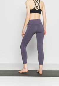 Fioletowe legginsy do ćwiczeń z wysokim stanem, o gładkiej fakturze i kontrastowymi szwami, w połączeniu z czarnym sportowym stanikiem na ramiączkach.