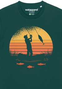 T-shirt en coton vert foncé avec une silhouette orange d'un coucher de soleil représentant une personne en train de pêcher, avec des poissons dessinés en dessous et des accents d'herbe.