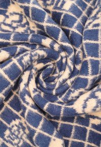 Coperta in lana navy e crema con un motivo a quadri testurizzato, caratterizzata da quadrati alternati e disegni intricati, arrotolata dolcemente a spirale.