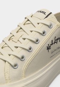 Αθλητικό παπούτσι από καμβά σε κρεμ απόχρωση με λευκά κορδόνια, μεταλλικά κουμπώματα, παχύ καουτσούκ πέλμα και μαύρο λογότυπο "Karl Lagerfeld" στην πλευρά και στη γλώσσα.