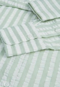 Camisa a rayas verde claro hecha de tela texturizada con rayas blancas, que cuenta con puños abotonados y un cuello limpio y doblado.