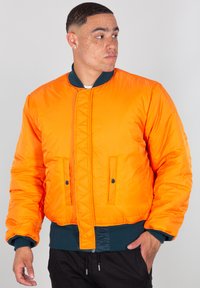 Oranžová bomber bunda s ribovaným zeleným límcem a manžetami. Obsahuje dvě přední kapsy a prošívaný přední panel. Hladká textura.