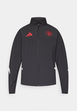 Black zip-up jacket with high collar, red Manchester United logo and three stripes on the left shoulder. Features white accents down the sleeves.
