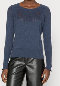 Granatowy sweter z dzianiny z teksturowanym karczkiem w diamentowe wzory, ściągaczami przy rękawach oraz okrągłym dekoltem. Gładkie wykończenie materiału.