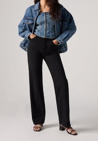 Veste en denim bleu clair, haut en denim court, pantalon large taille haute noir et sandales à talons avec lanières noires.