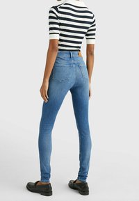 Smala blå jeans med hög midja, tillverkade av denim. Har två bakfickor och en brun läderlapp i midjan.