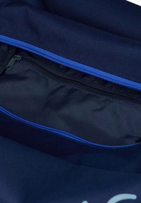 Innenseite eines marineblauen Rucksacks mit einem glatten, dunklen Stofffutter. Verfügt über einen leuchtend blauen Reißverschluss und eine zusätzliche schwarze Reißverschlusstasche.
