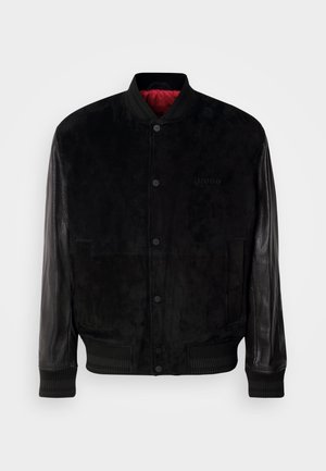 Bomber negro con cuerpo de ante y manguitos de piel, puños y dobladillo acanalados, cierre de botón a presión y forro interior rojo.