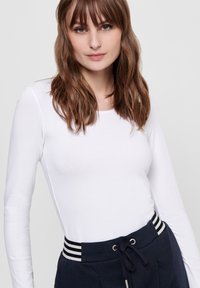 Weißes Langarmoberteil mit rundem Halsausschnitt und glatter Textur, kombiniert mit marineblauen Hosen mit gestreiftem elastischem Bund.