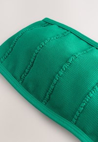 Roheline soonikuline tekstiilkate, millel on tikkimistega kaunistatud tikitud sektsioonid ja sile, ümar serv. Pehme kangapind.