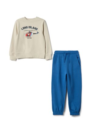 Beige sweatshirt met "LONG ISLAND" opdruk en helikopterontwerp; gecombineerd met blauwe joggers met elastische taille en omgeslagen enkels.
