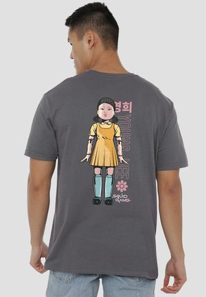 Gray cotton t-shirt featuring a colorful graphic of a girl in a yellow dress and blue boots with the text “YOUNG HEE” and “SQUID GAME.”
