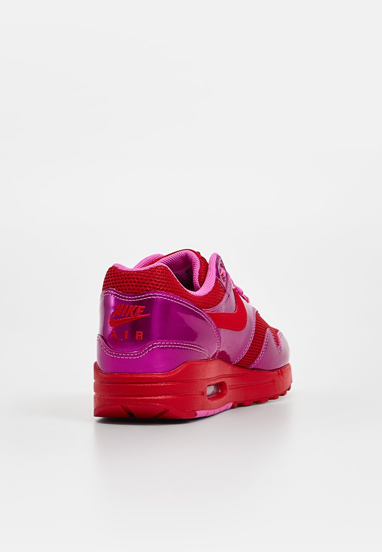 Baskets Nike Air en rose vif et rouge, avec une finition brillante, des accents en mesh et une bulle d'air visible dans la semelle.